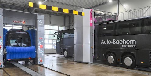 Ein Bus wird in einer Garage gewaschen, während Wasser und Seife auf die Karosserie gesprüht werden.
